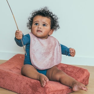 Baby op een kussen draagt een Timboo waterdicht slabbetje in Misty Rose