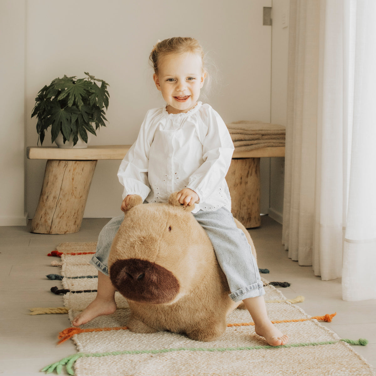 Wild & Soft Bouncy Capybara, peuter zit lachend op het bruine springdier in een lichte kamer