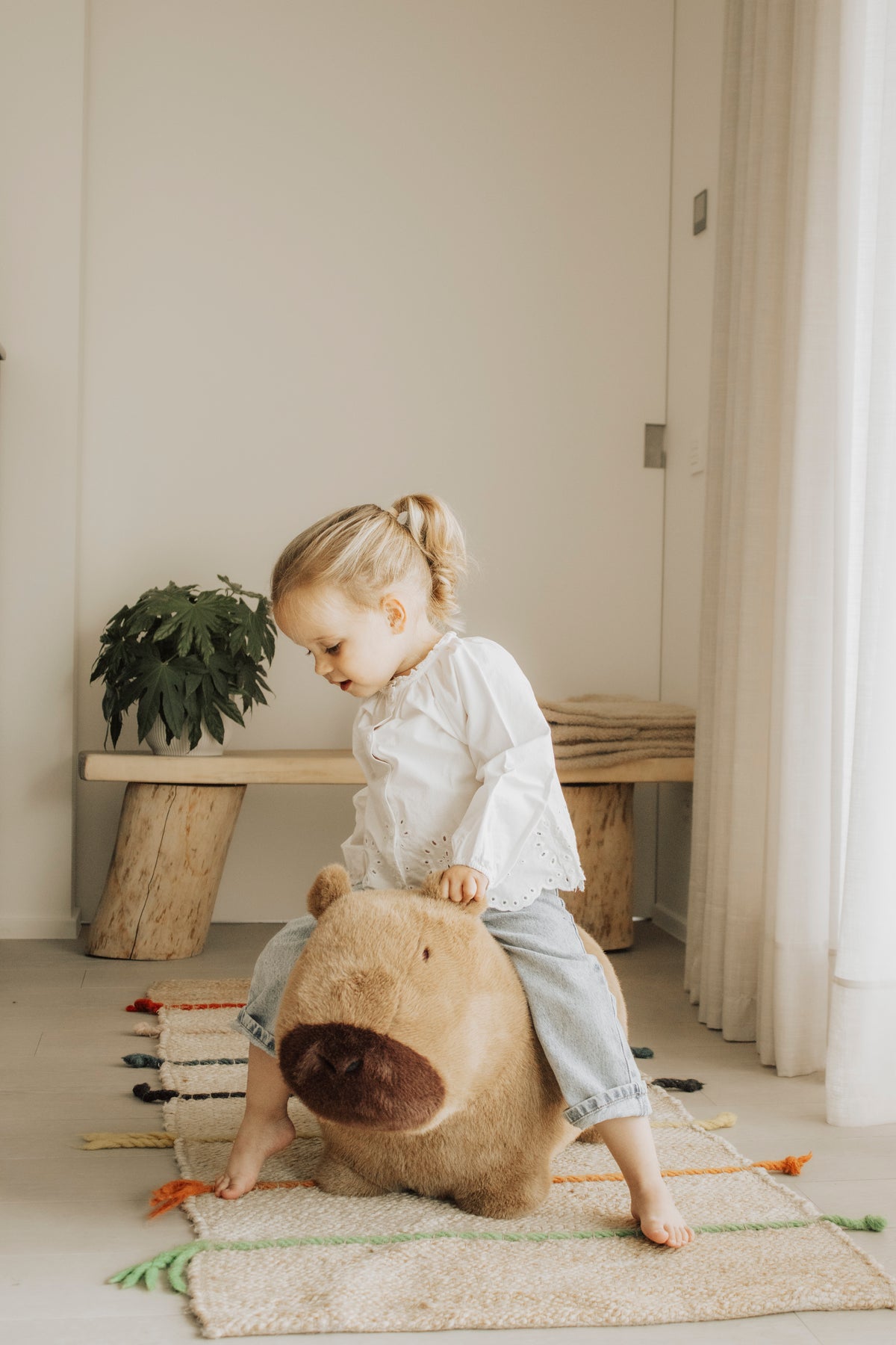 Wild & Soft Bouncy Capybara, peuter zit lachend op het bruine springdier in een lichte kamer