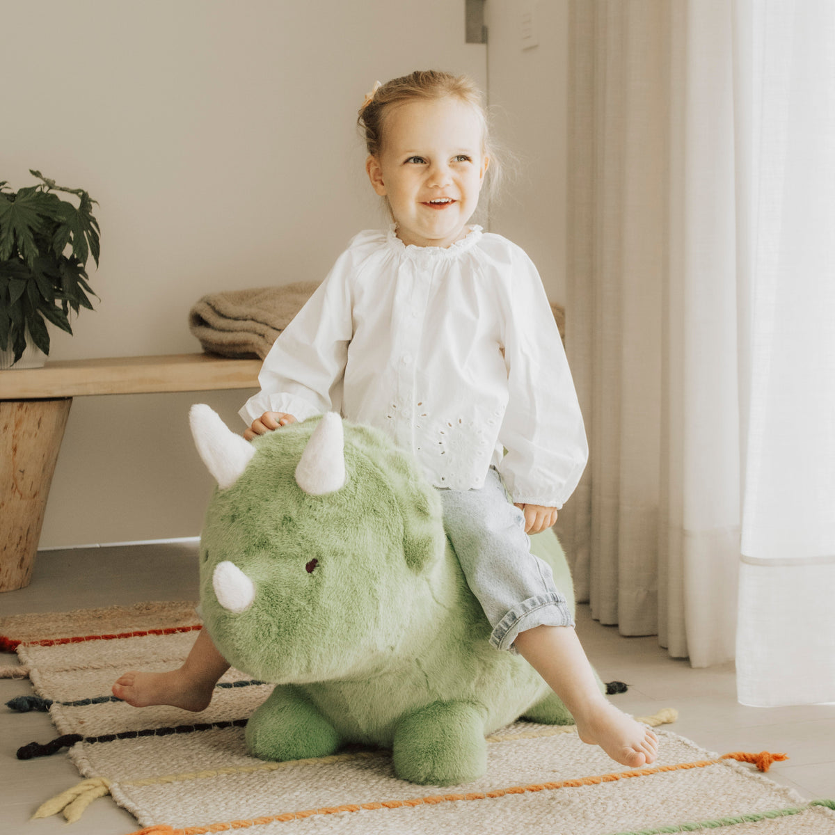 Wild & Soft Bouncy Dino, meisje zit lachend op de groene dino met witte hoorns