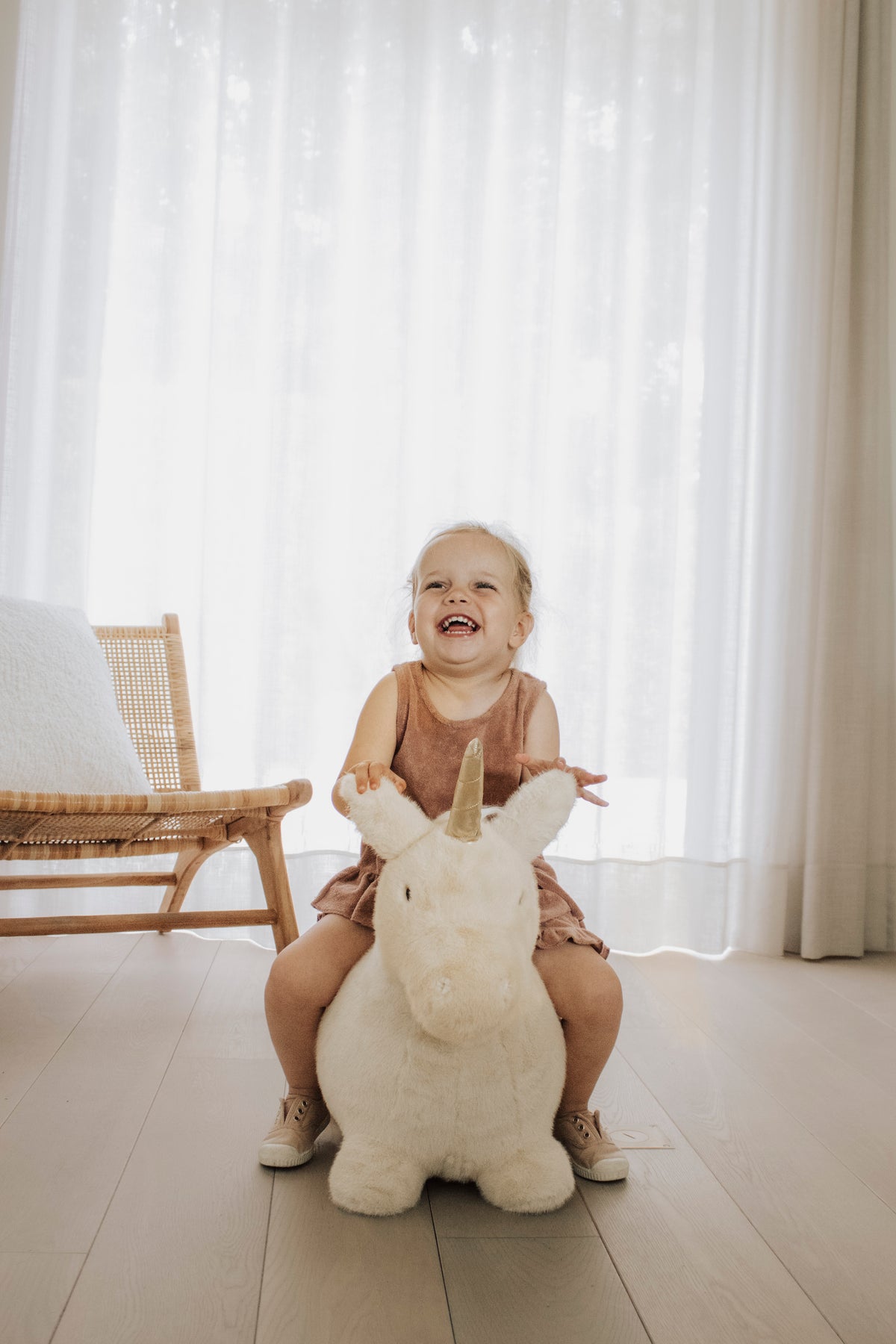 Wild & Soft Bouncy Eenhoorn, meisje zit lachend op de crèmekleurige eenhoorn