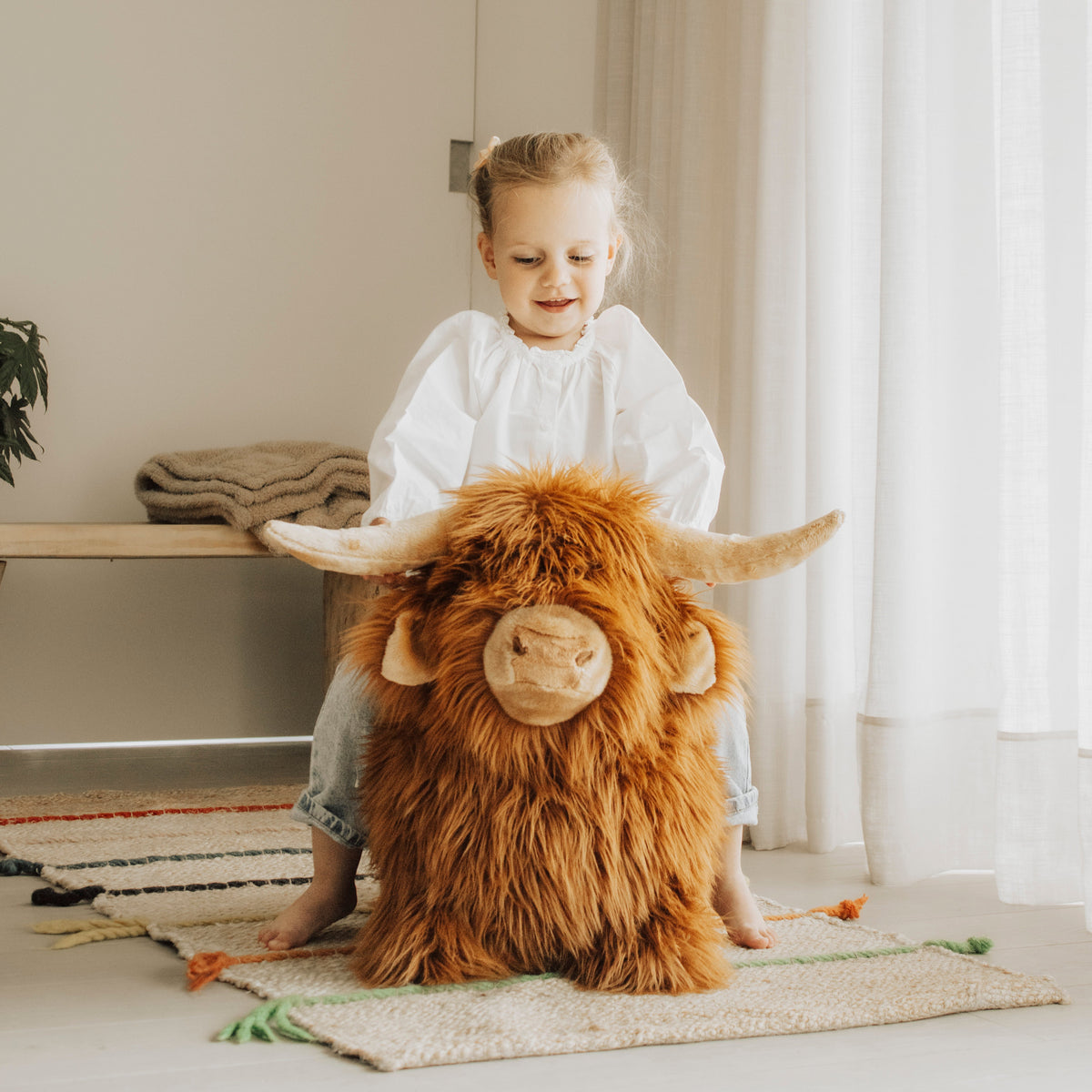Wild & Soft Bouncy Highland Koe, meisje zit op het bruine springdier met lange vacht en hoorns