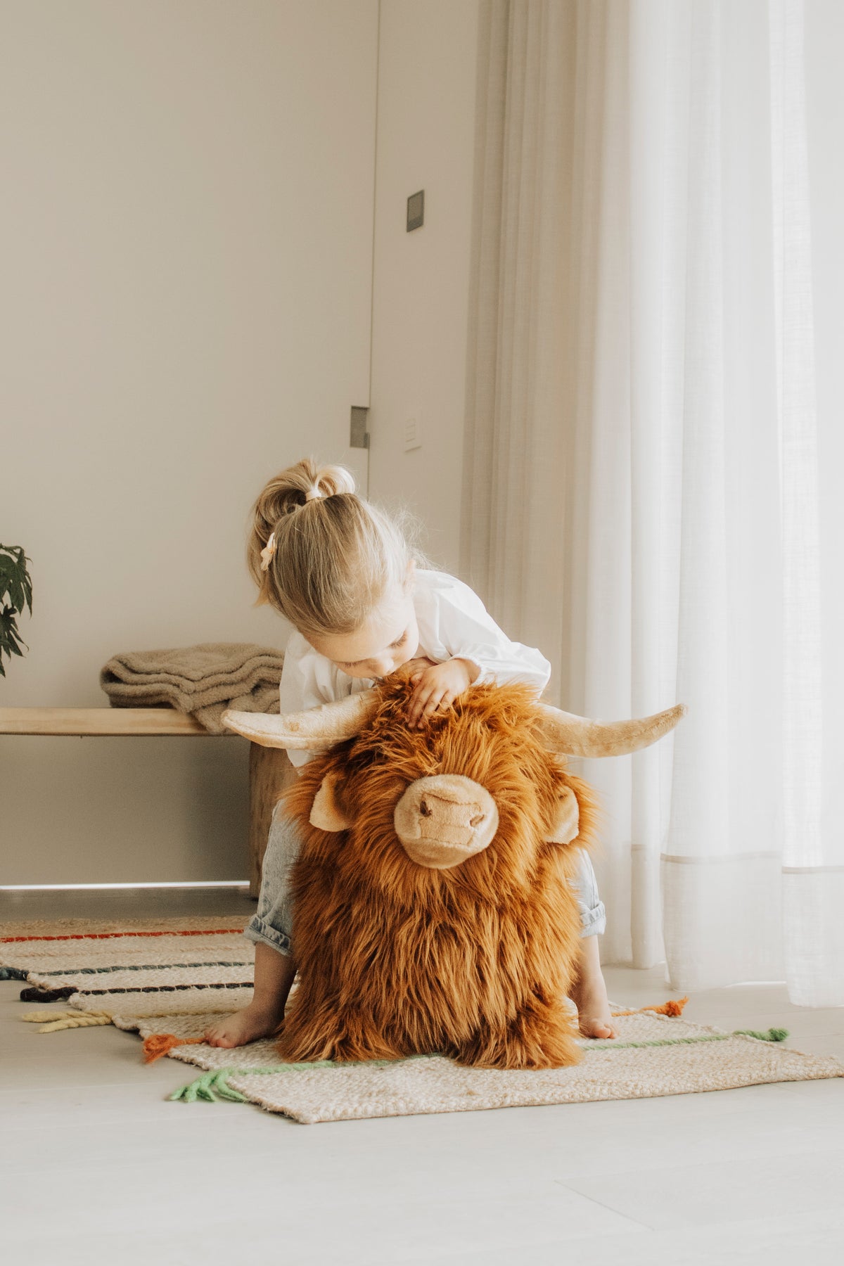 Wild & Soft Bouncy Highland Koe, meisje zit op het bruine springdier met lange vacht en hoorns